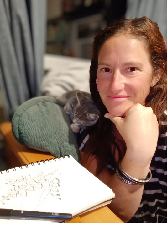 Jess poses with her cat, a sketchbook lays in front of her.